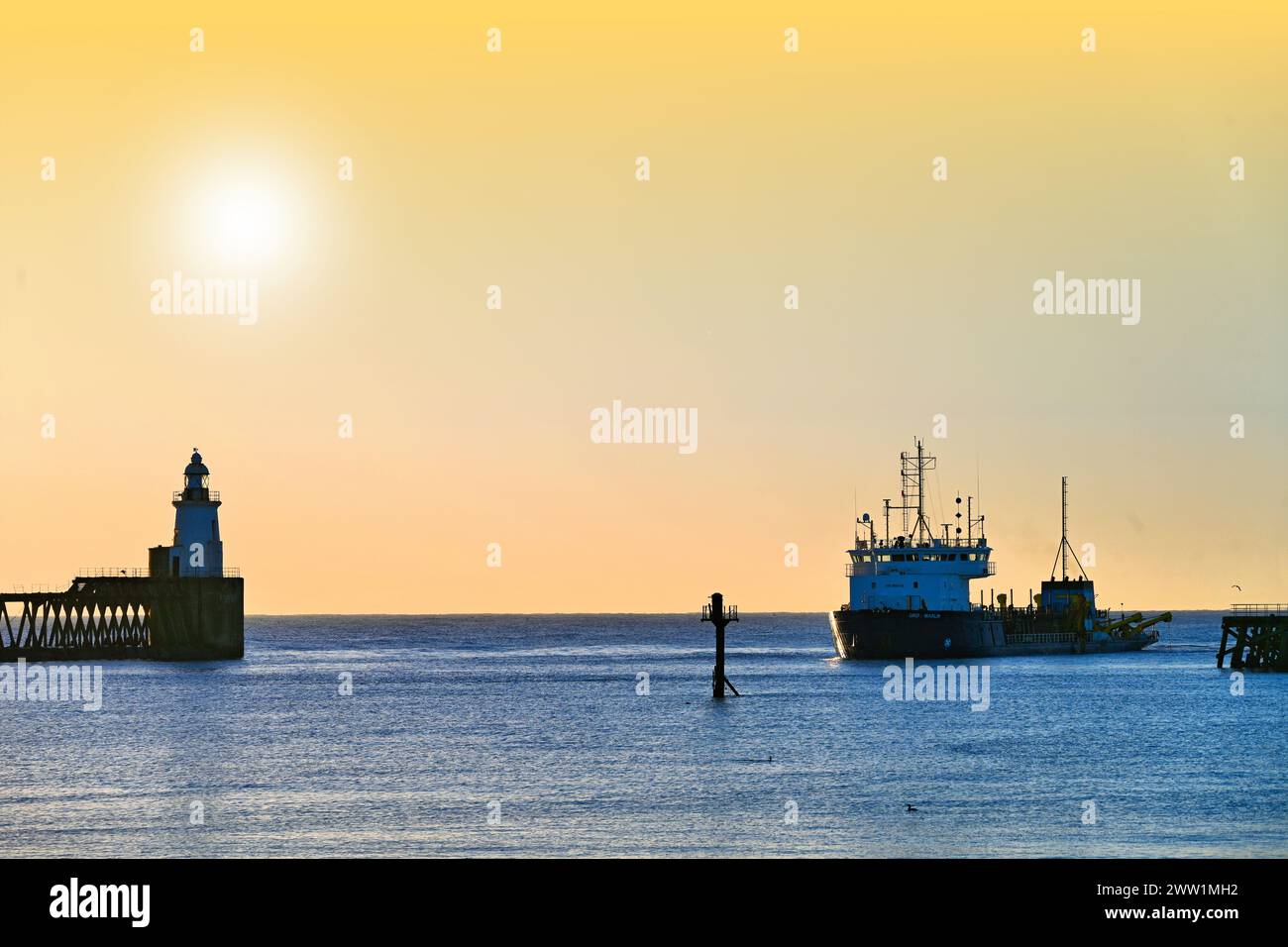 Suction dredger UKD Marlin working at Blyth harbour  Northumberland early dawn against orange sky Stock Photo