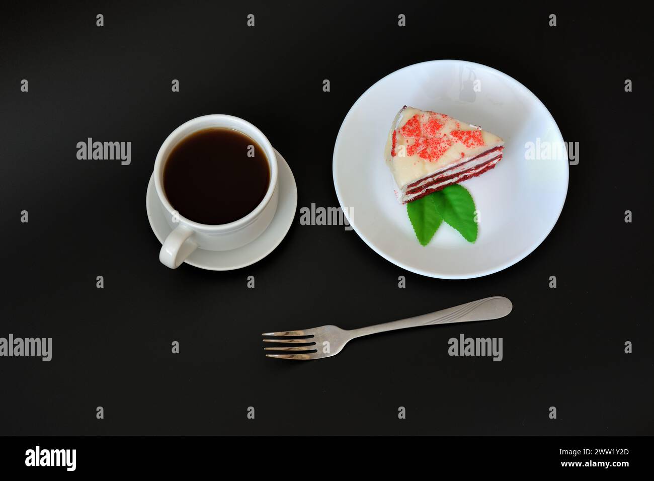 A plate with a piece of Red velvet cake, a fork and a cup of hot black coffee on a black background. Top view, flat lay. Stock Photo