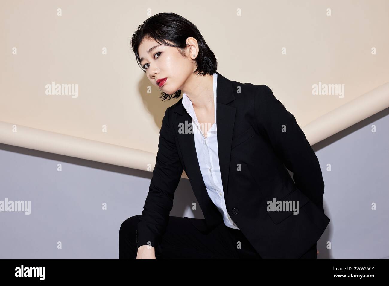 A woman in a business suit standing against a wall Stock Photo