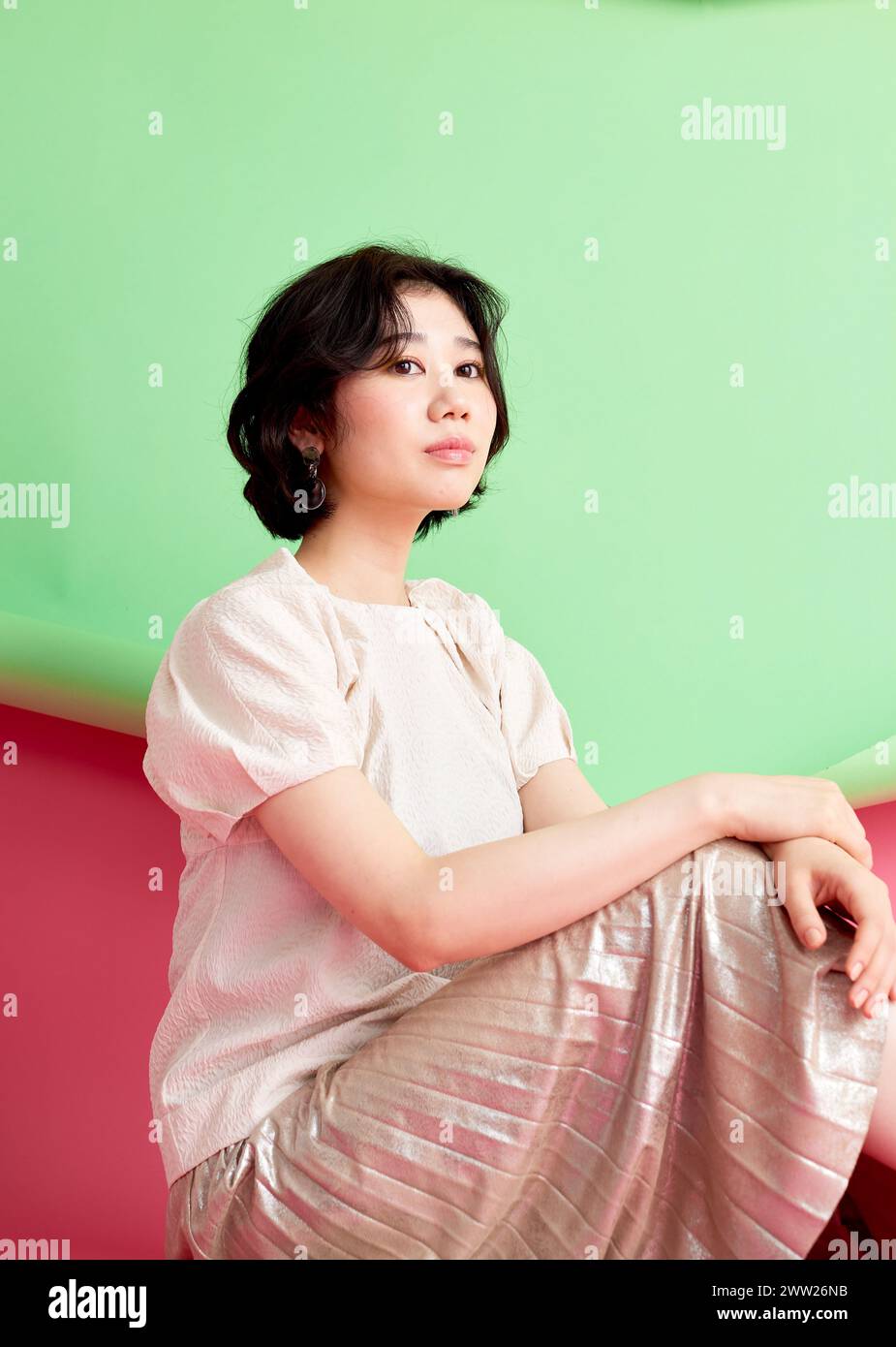 A woman sitting on a pink and green background Stock Photo