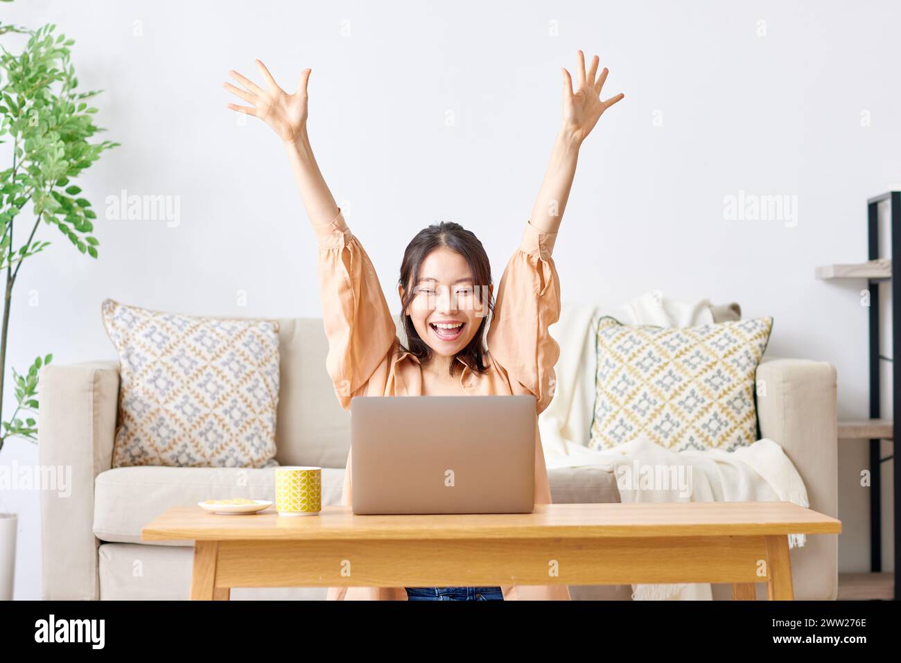 A woman sitting on a couch with her arms up and a laptop Stock Photo