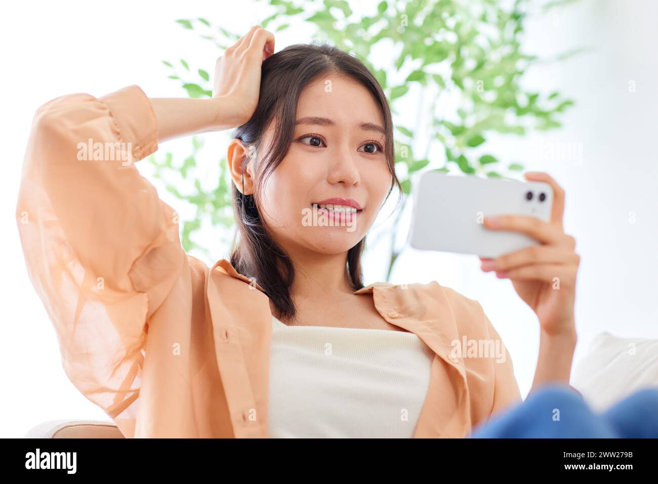 Asian woman sitting on couch holding her phone Stock Photo