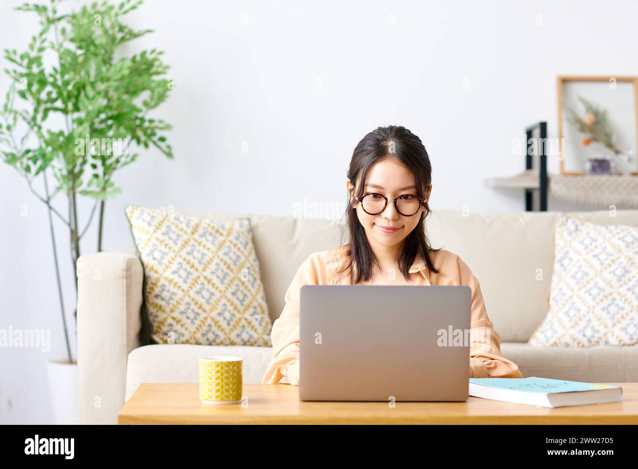 A woman in glasses sits on a couch with a laptop Stock Photo