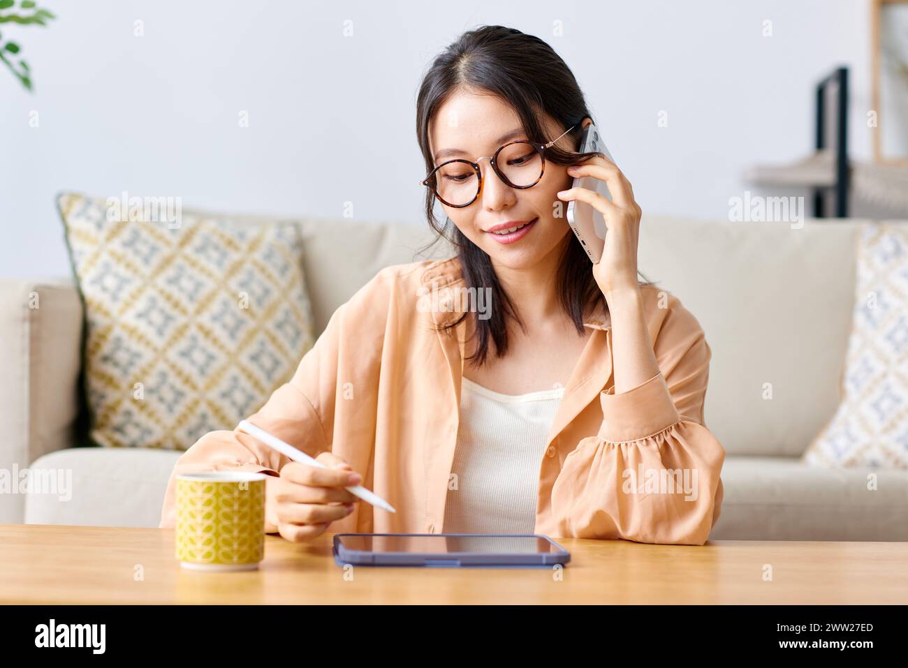 A woman in glasses sits at a table with a cup of coffee and a tablet Stock Photo