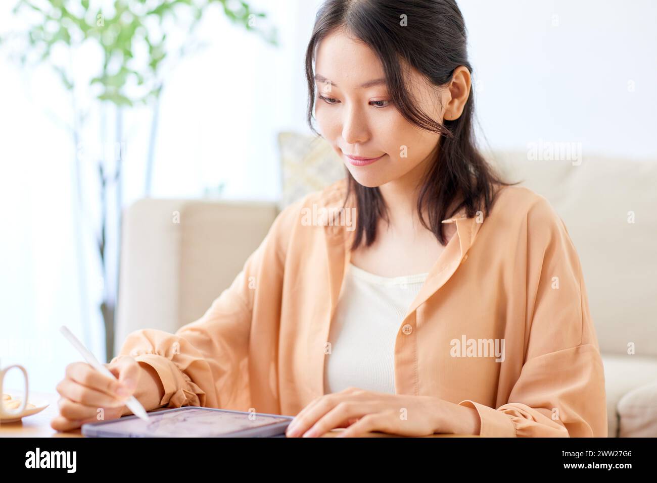 Asian woman writing on tablet while sitting at table Stock Photo