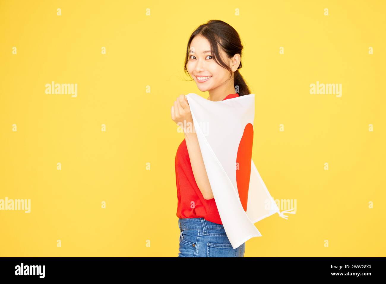 A woman holding a Japanese flag over a yellow background Stock Photo