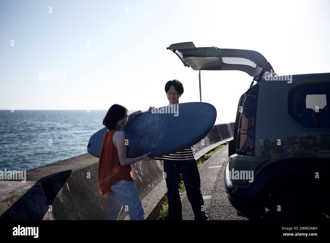 A man and a woman standing next to a car with a surfboard Stock Photo
