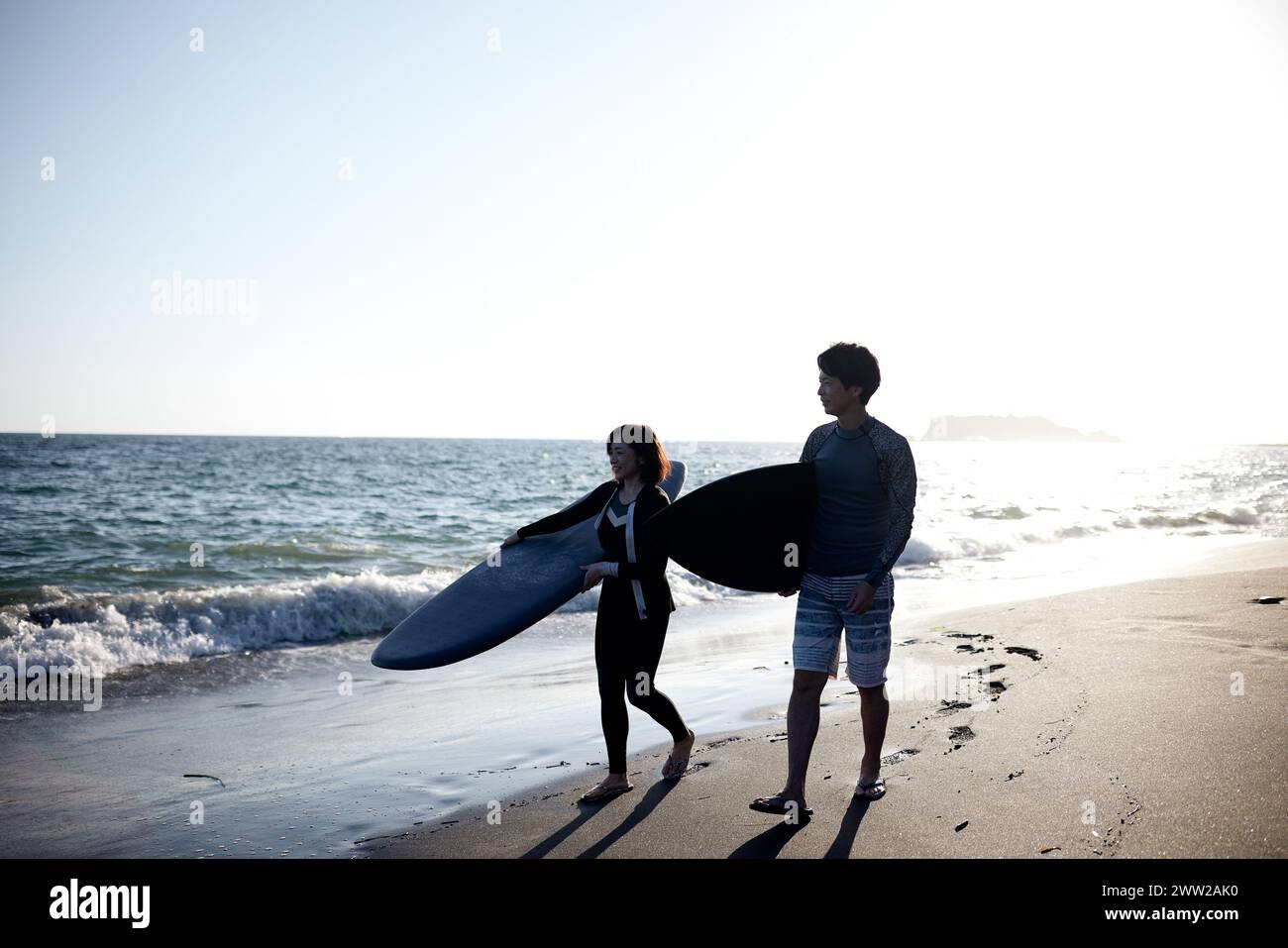 A man and a woman walking on the beach holding surfboards Stock Photo