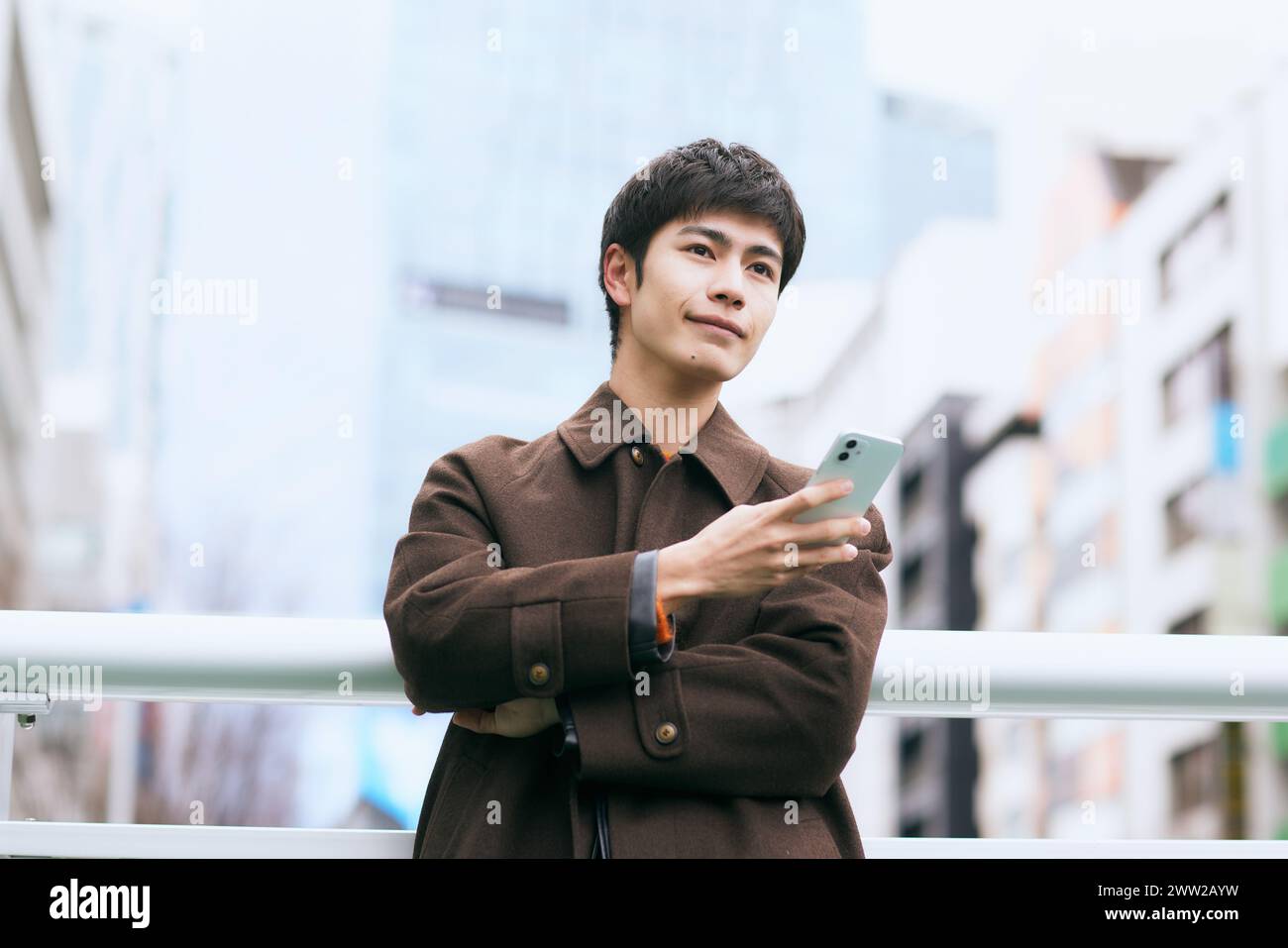 Asian man in coat holding phone in city Stock Photo