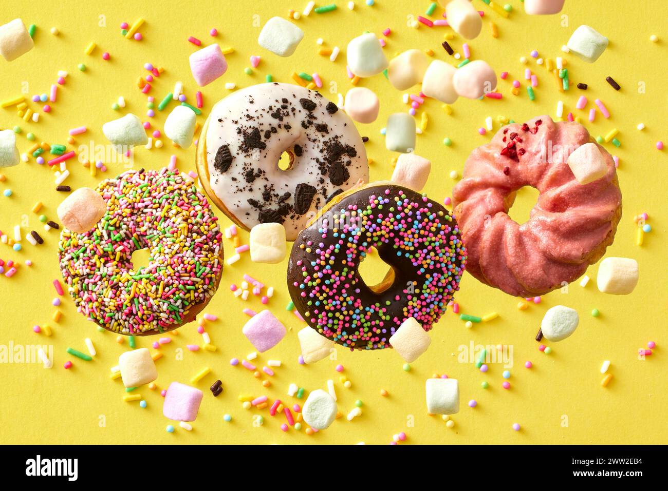 Four donuts with sprinkles on a yellow background Stock Photo