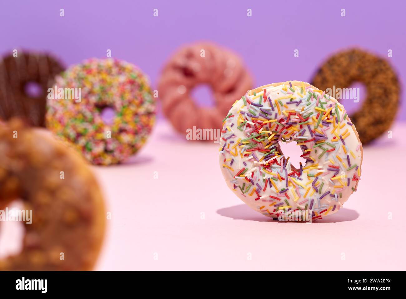 A group of donuts with sprinkles on a pink background Stock Photo - Alamy