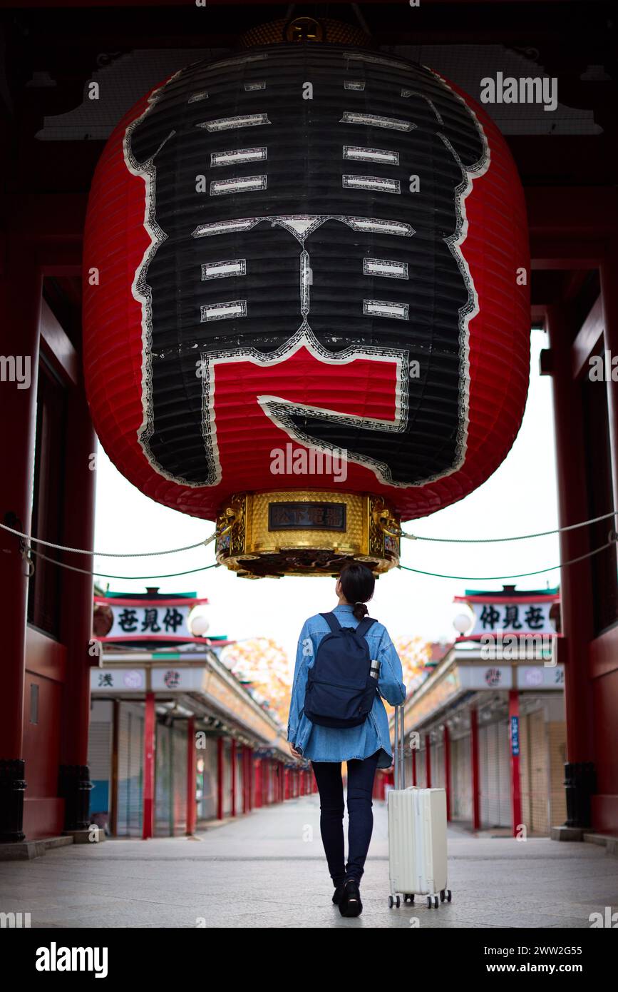 A woman walking down a temple street with a suitcase Stock Photo