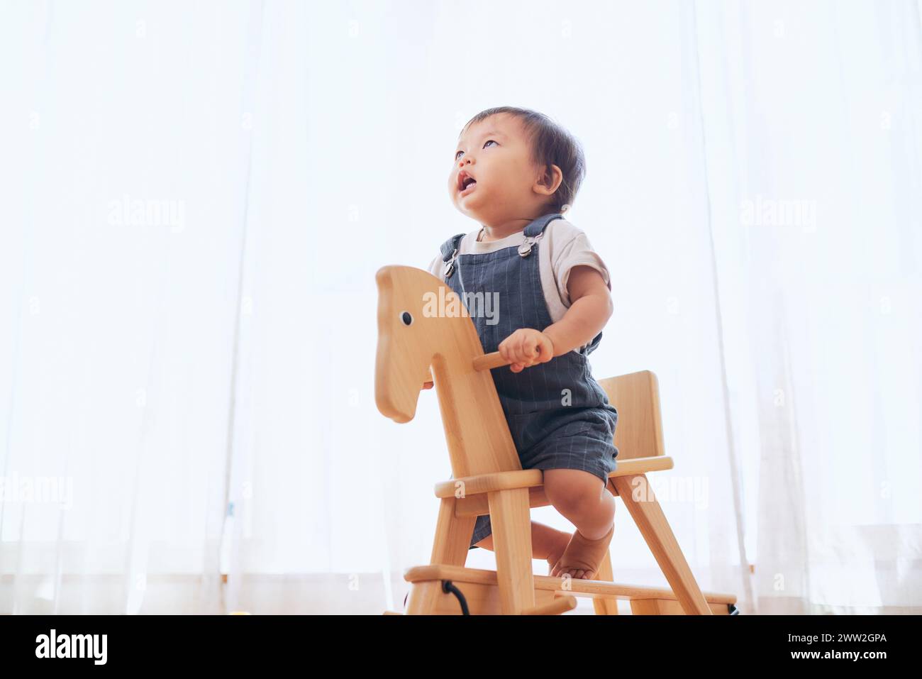 A baby riding a wooden horse in a room Stock Photo