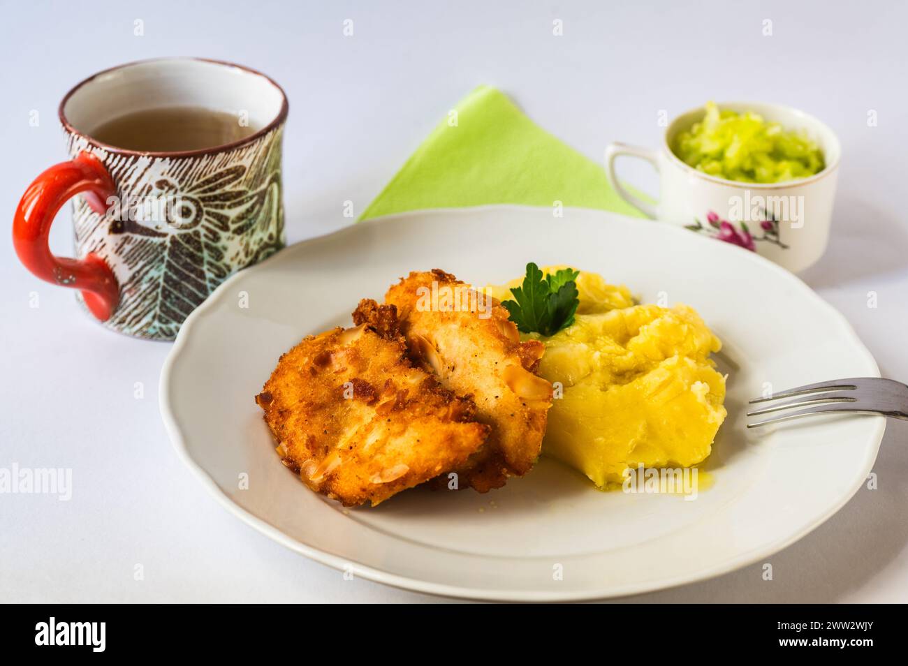 Fried schnitzel in breadcrumb with almonds, mashed potato on white plate, green towel,decorative cup with lemonade,cucumber salad. Stock Photo