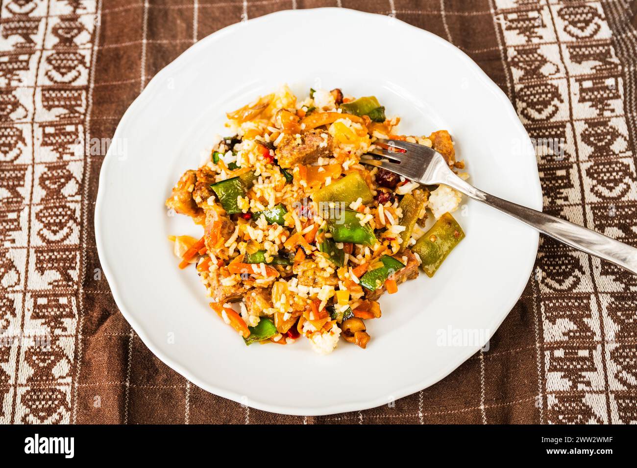 Vegetarian risotto with mushroom, pea pod and vegetable, fork on plate on tablecloth. Stock Photo