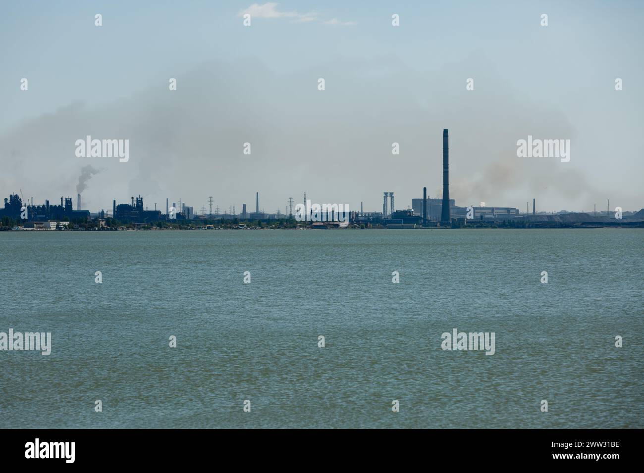 Industrial skyline dominated by metallurgical plant across water, emitting smoke into sky. Factory pollution, environmental concerns, and heavy Stock Photo