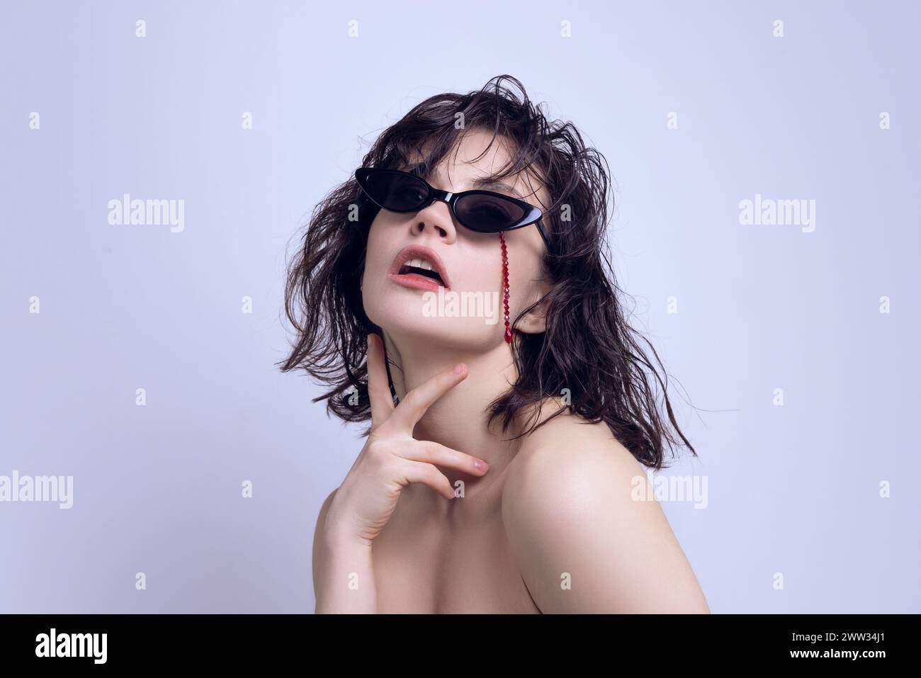 Beautiful young woman with wet hair wearing sunglasses, red beads draped over face. Emerging fashion trends. Stock Photo
