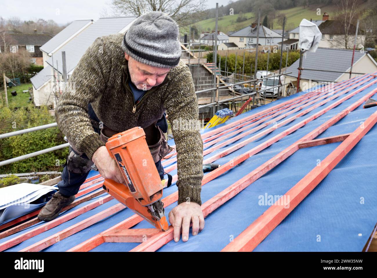 Roofer using a nail gun to fix batons on a new house roof, Llanfoist, Wales, UK Stock Photo