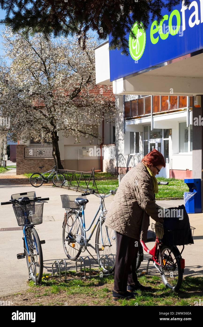 older woman with bicycles in cycle rack outside of eco family mini market store lenti zala county hungary Stock Photo