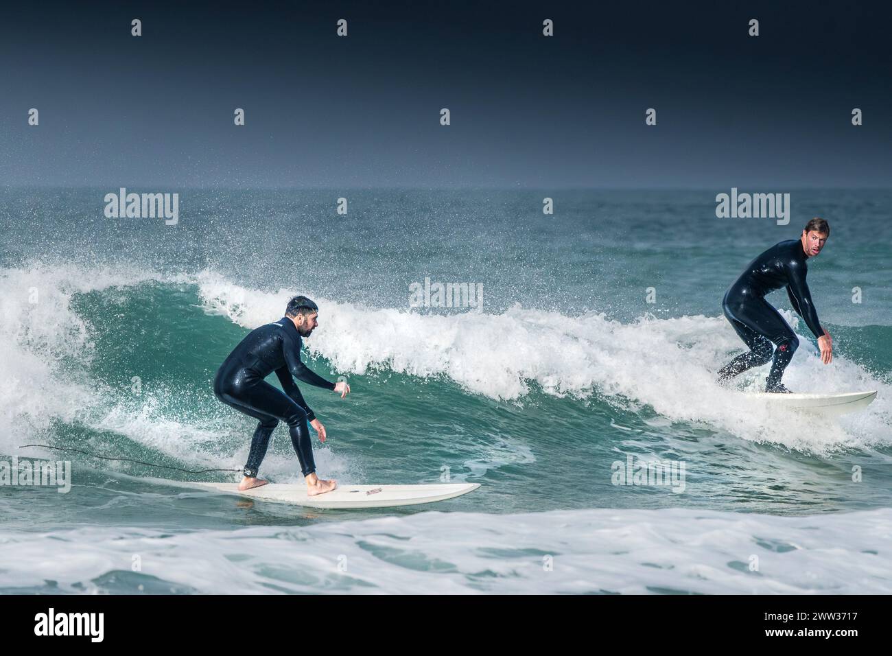 Two surfers riding a wave at Fistral in Newquay in Cornwall in the UK ...