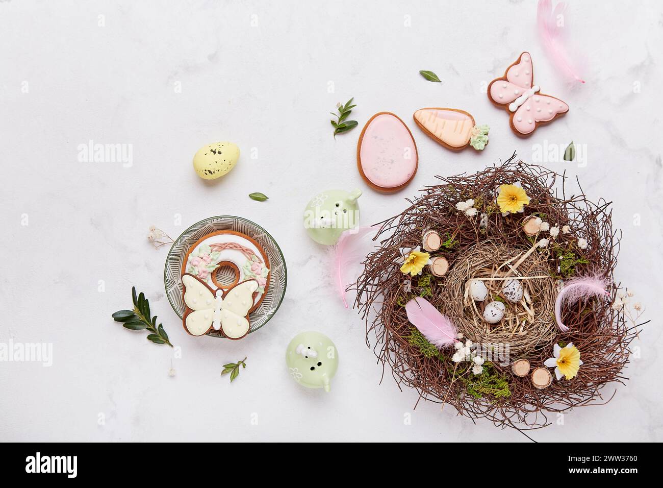 Easter table setting decorations - nest and pastel Easter cookies on white background aesthetics. Stock Photo
