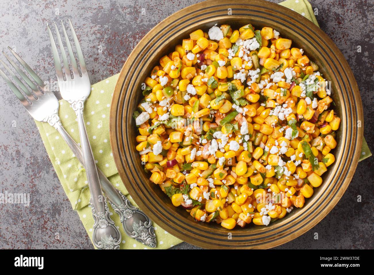 Mexican street corn snack Esquites with added sauce, chili, onion and cheese close-up in a plate on the table. Horizontal top view from above Stock Photo