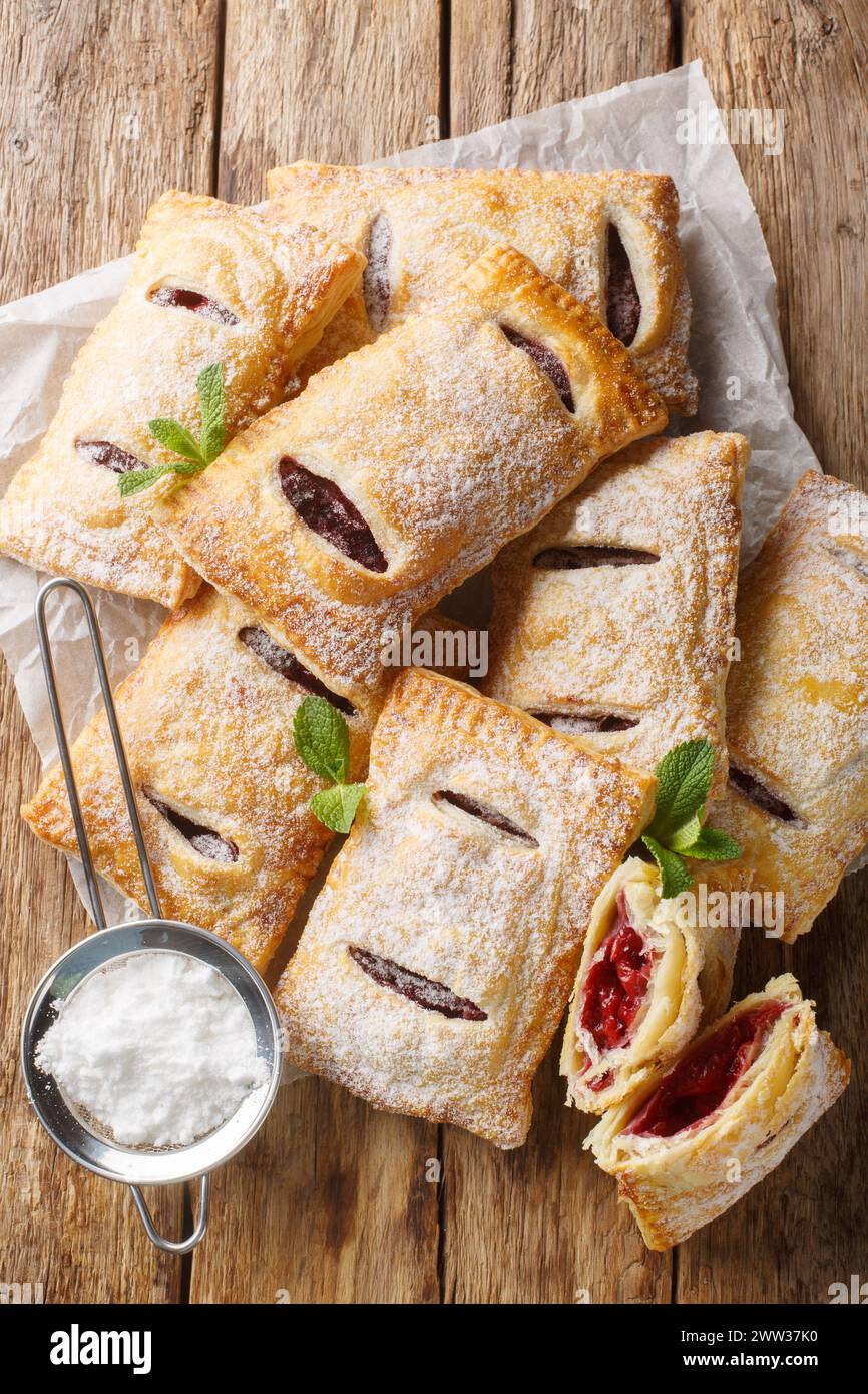 Cherry puff pastry with powdered sugar and mint close-up on the table. Vertical top view from above Stock Photo