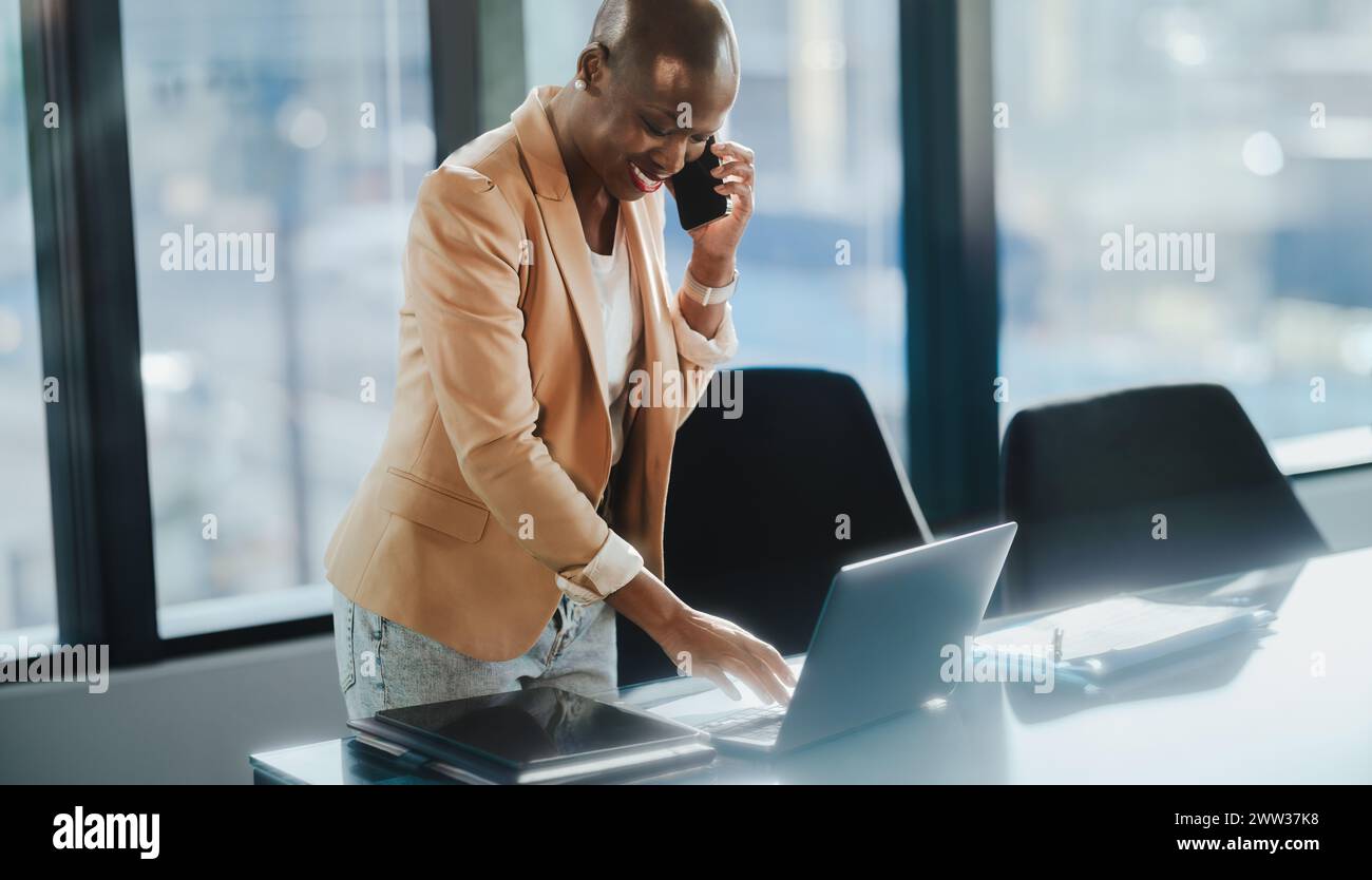 Business woman in an office, discussing and talking on her smartphone. She uses a laptop and tablet to work, reflecting her professionalism and succes Stock Photo