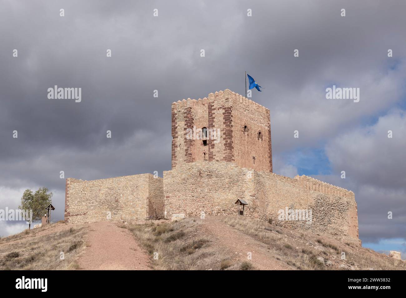 ancient stone castle with a blue flag atop, surrounded by a cloudy sky ...