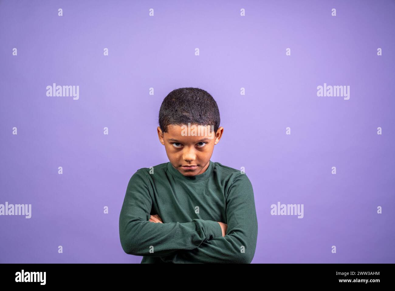 A young boy is standing with his arms crossed and looking down. He is upset or angry Stock Photo