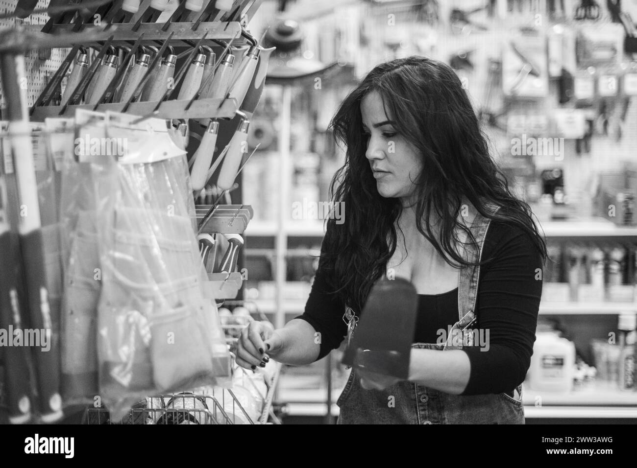 Hispanic worker Woman concentrating on selecting a tool in a monochrome hardware store setting Stock Photo
