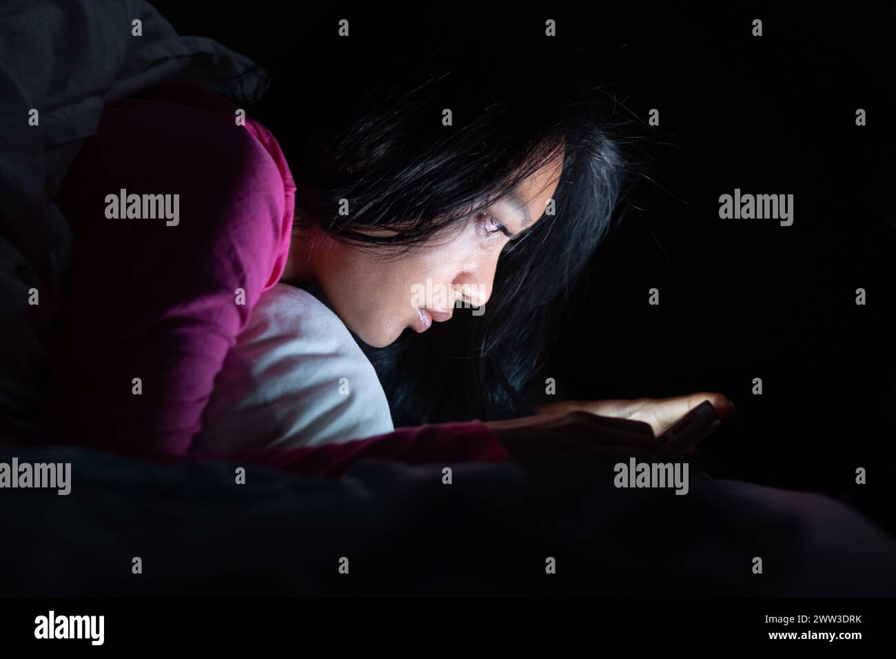 A young woman is lying in bed and using a smart phone Stock Photo