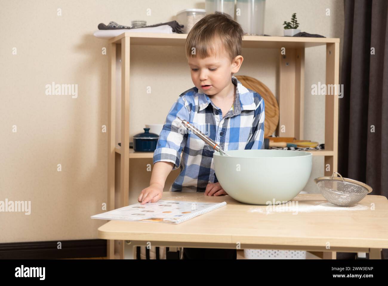 Little boy making pastries according to the recipe book for toddlers