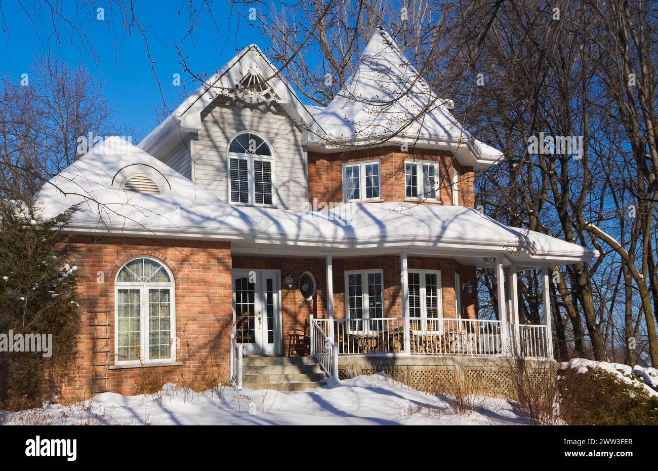 Two story red brick Victorian style home with white trim and landscaped front yard in winter, Quebec, Canada Stock Photo