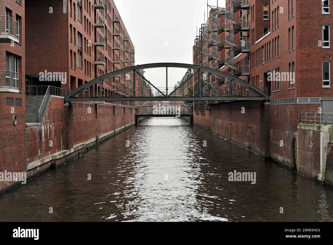 A pedestrian bridge over a water channel with brick buildings on the sides, Hamburg, Hanseatic City of Hamburg, Germany Stock Photo