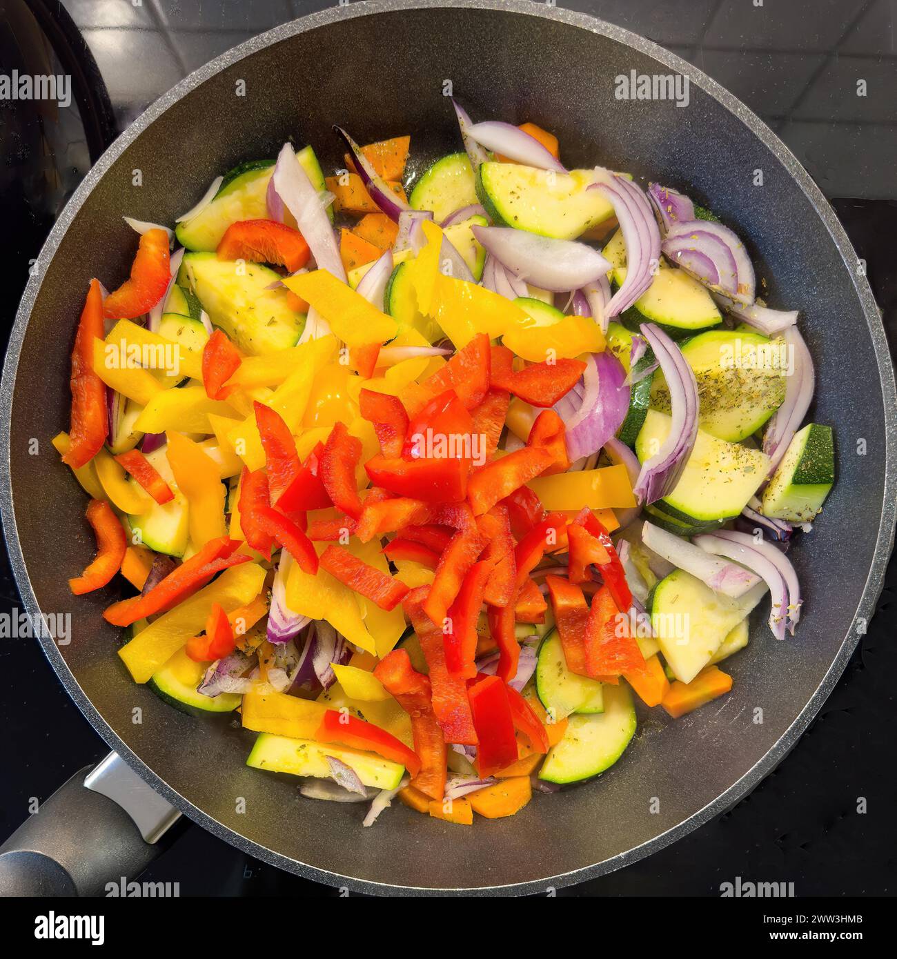 Vegetarian vegan dish Vegetable pan with courgettes red yellow peppers onions vegetable onions carrots carrots Vegetables are sauteed with olive oil Stock Photo
