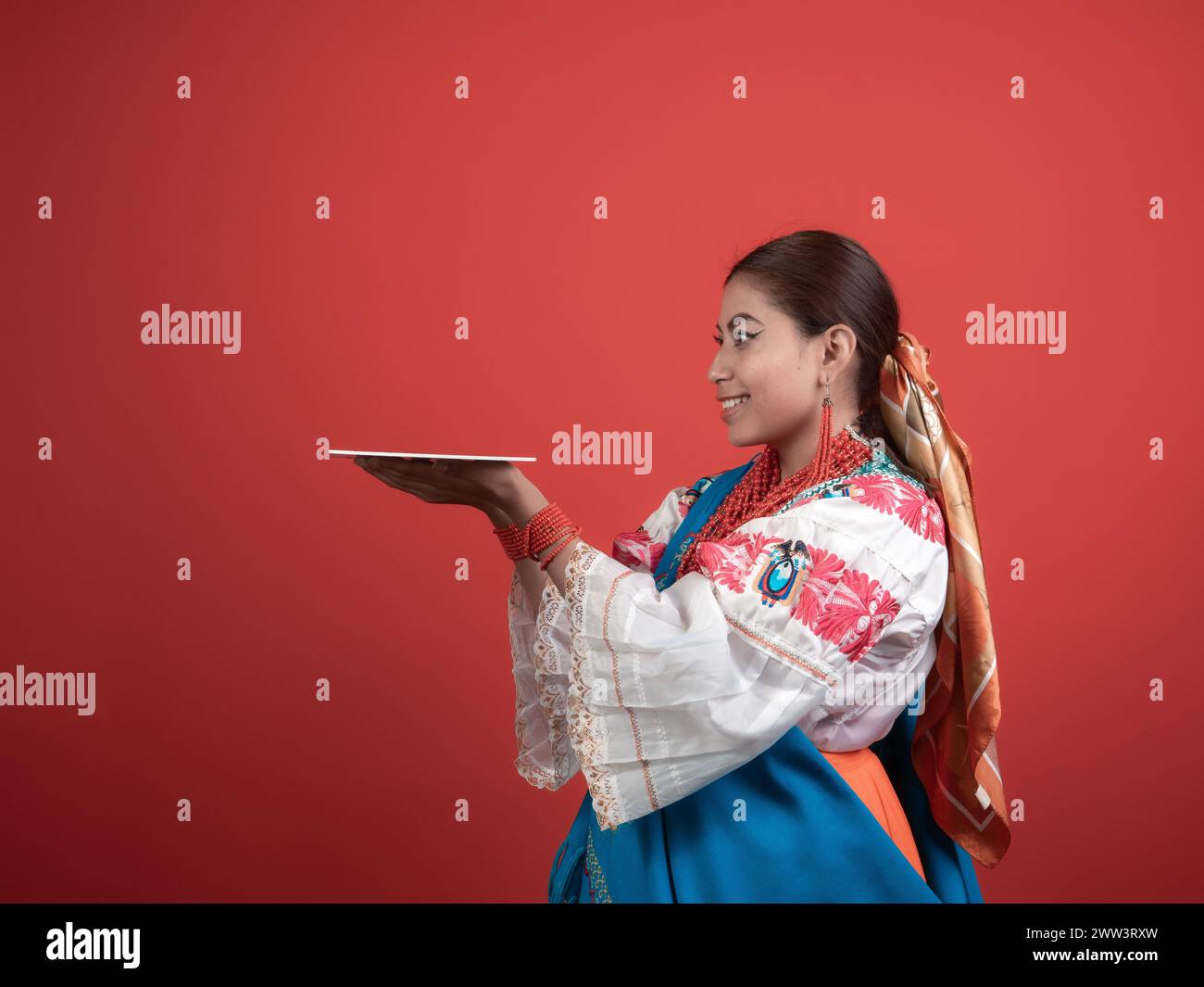 Hispanic girl of Kichwa origin with a red background and holding a plaque to place an object. Stock Photo