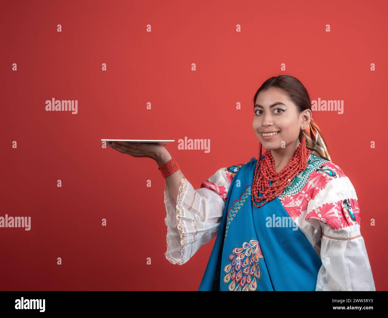 Hispanic girl of Kichwa origin with a red background and holding a plaque to place an object. Stock Photo