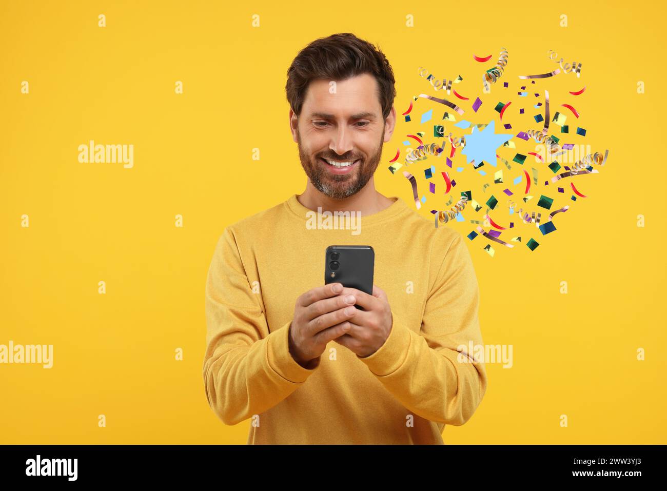 Discount offer. Happy man holding smartphone on yellow background. Confetti and streamers near him Stock Photo