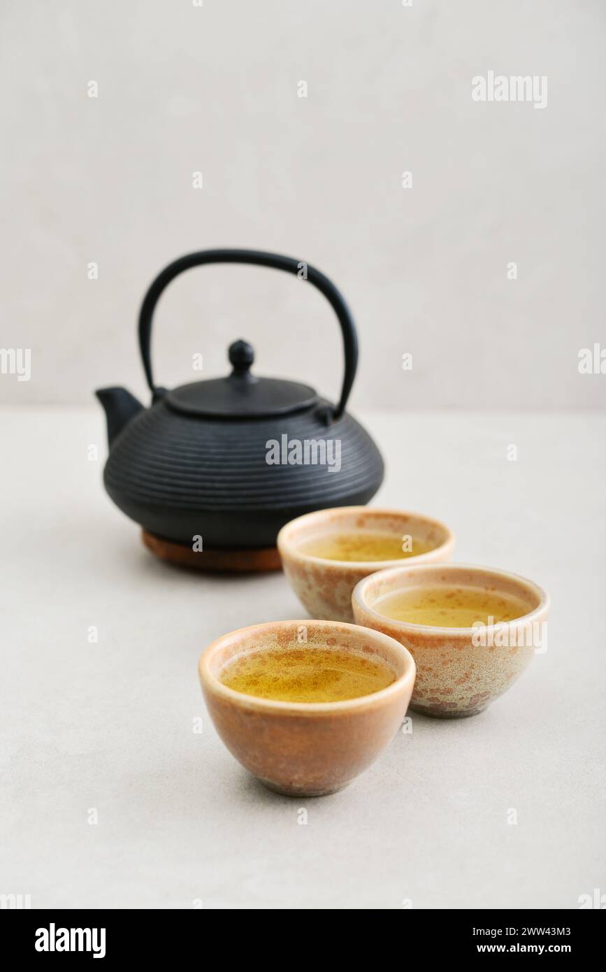 Black cast iron teapot and three ceramic cups of green tea on a light background Stock Photo