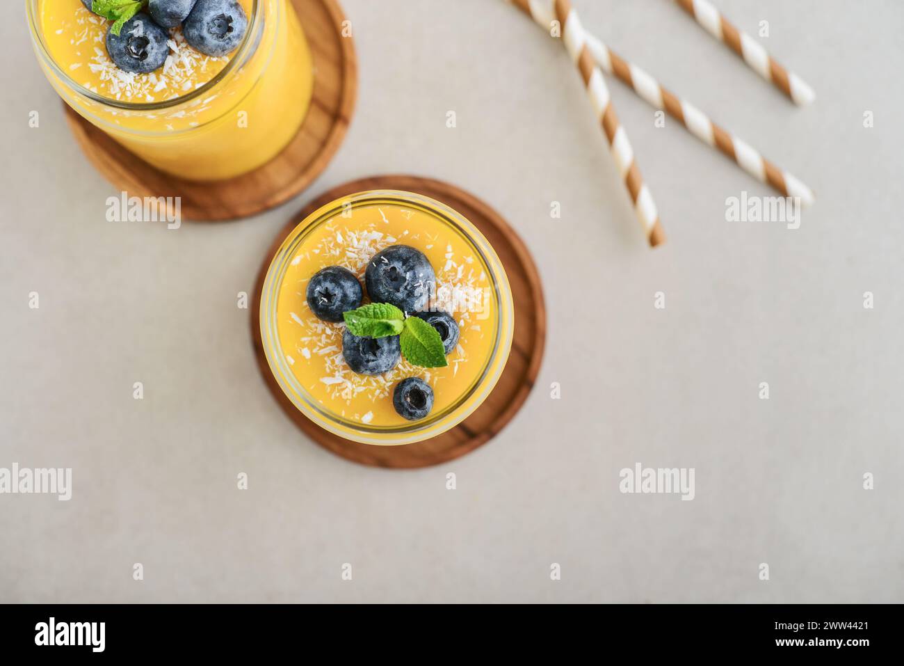 Refreshing and healthy mango smoothie with coconut flakes and fresh blueberries on light background, top view Stock Photo
