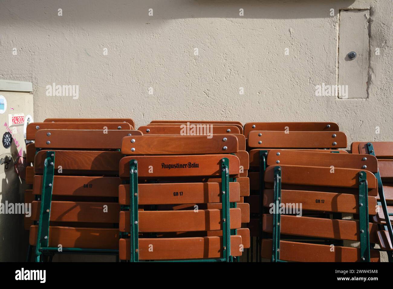 Biergartenstühle an Hauswand Zusammengeklappte Biergarten Stühle lehnen an Hauswand in der Frühlingssonne. Schriftzug Augustiner Bräu. München *** Bee Stock Photo