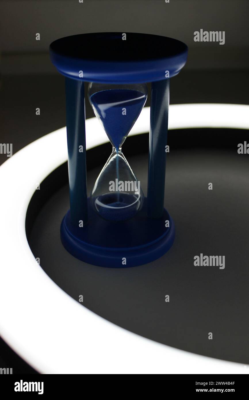 Plastic body of blue time glass with sand pouring inside in ring lamp Stock Photo