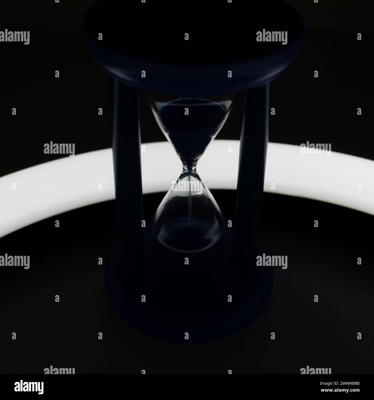 Illuminated Trickle Of Sand Inside Hourglass In Darkness Closeup View Stock Photo