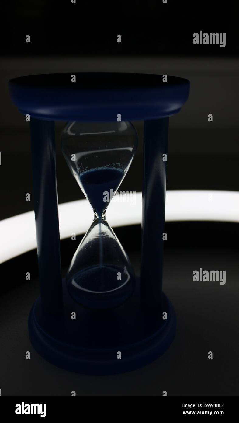 Sandglass with falling sand with soft backlight by curved lamp Stock Photo