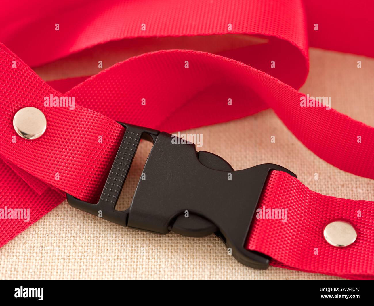 A black contoured side release plastic buckle with red nylon belt on a beige textile background Stock Photo
