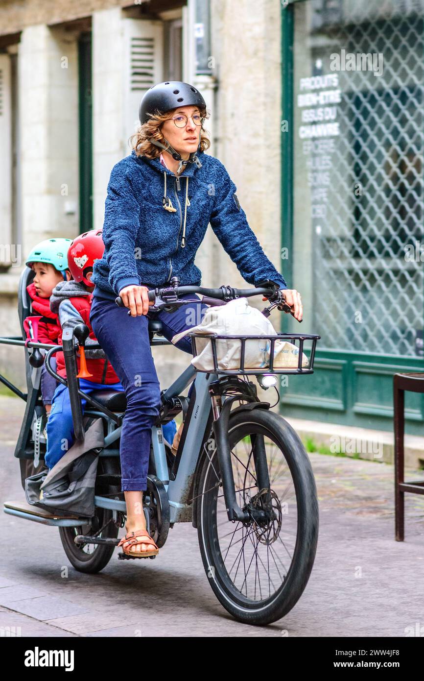 Mother riding BTWin electric assist bicycle with two young children in rear seats - Tours, Indre-et-Loire (37), France. Stock Photo