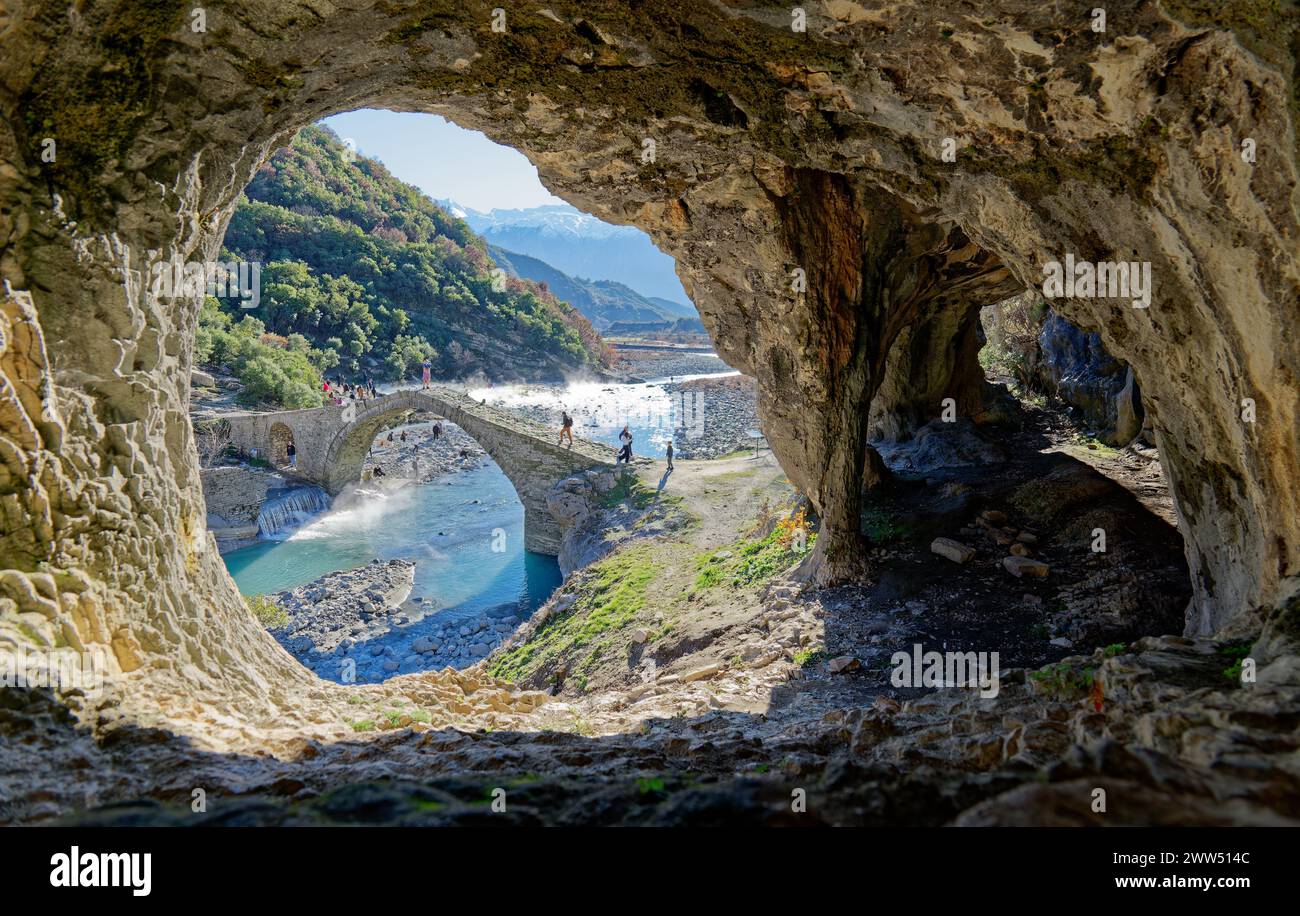 View from inside of the cave of the Kadiut Bridge in Benje, Permet, Albania. Stone bridge over the river. People crossing the bridge. Stock Photo