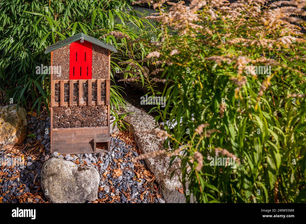 One red wooden insect house in the garden. Bug hotel at the park with plants. Outdoors. Stock Photo