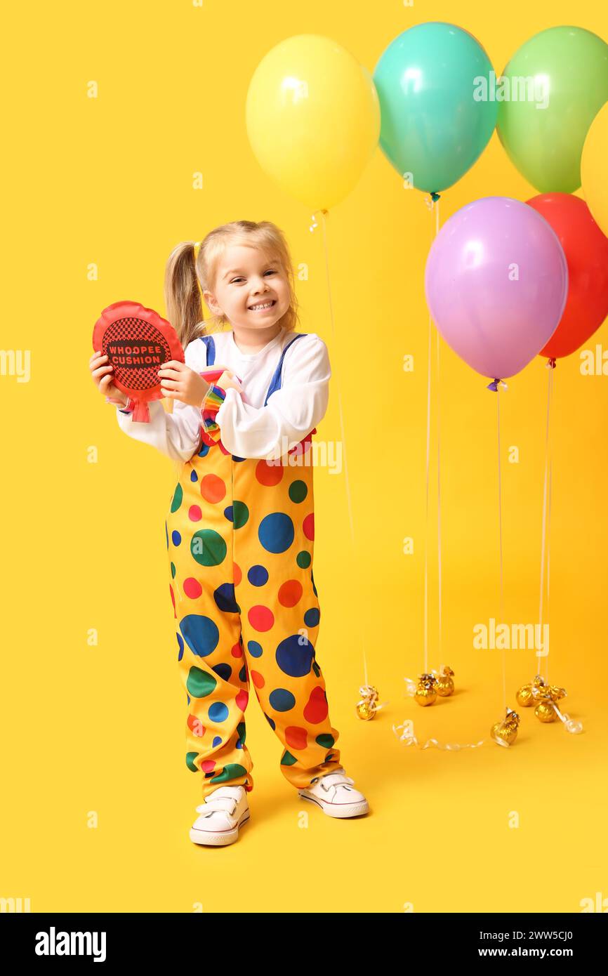 Cute little girl with whoopee cushion and balloons on yellow background ...